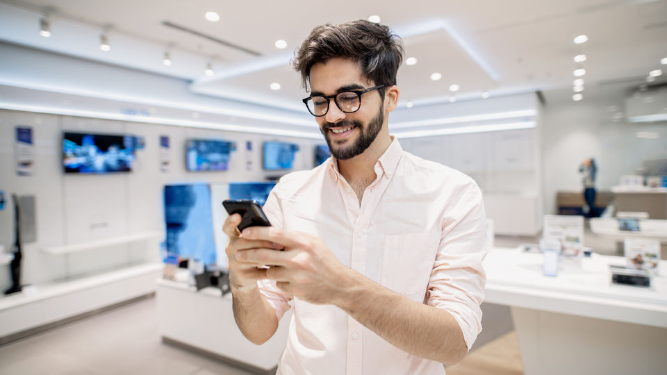 smiling male shopper choosing a new cellphone in a retail electronics store
