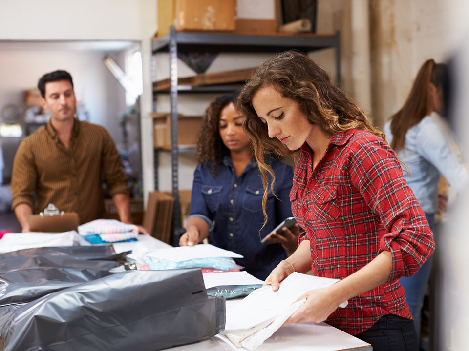 female store employee working in retail back room preparing inventory for display on the sales floor while a male and female employee observe