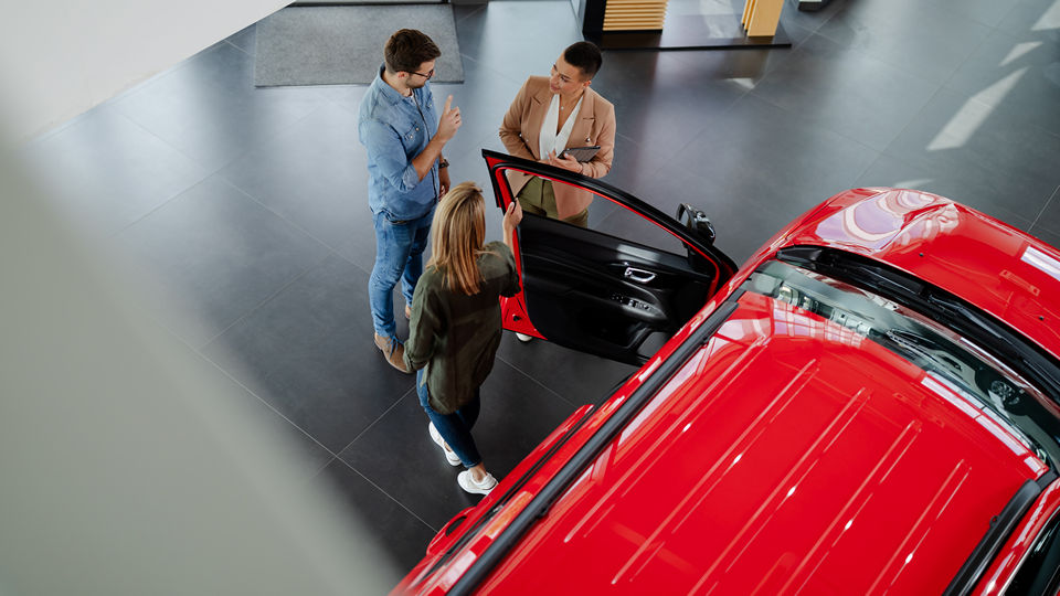 overhead view of an auto dealership sales floor with a male and female couple speaking with a female salesperson