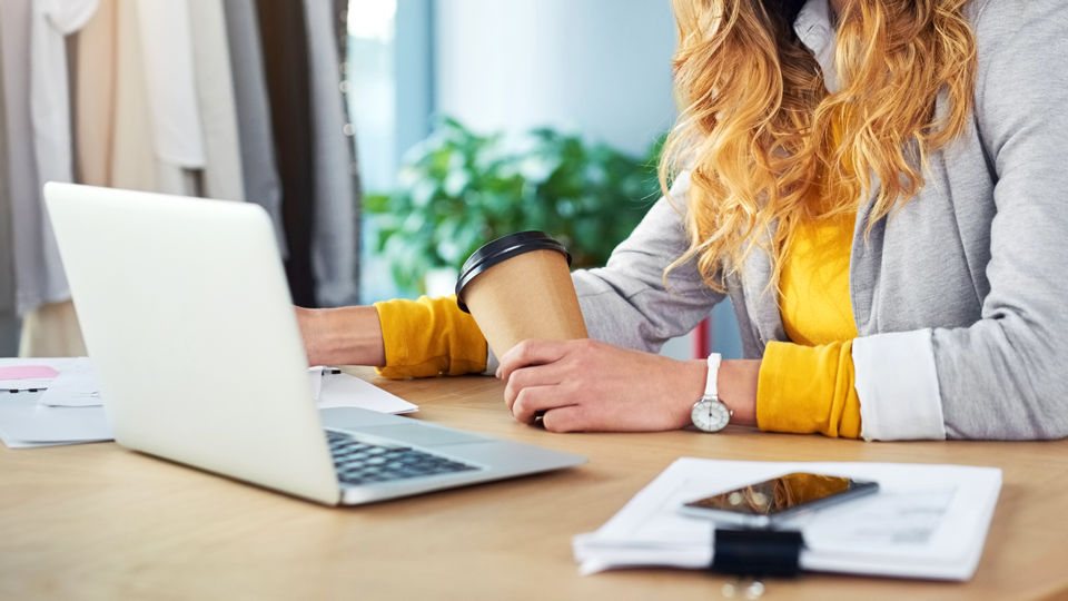 woman retail store manager in store office with phone and laptop reviewing store performance data