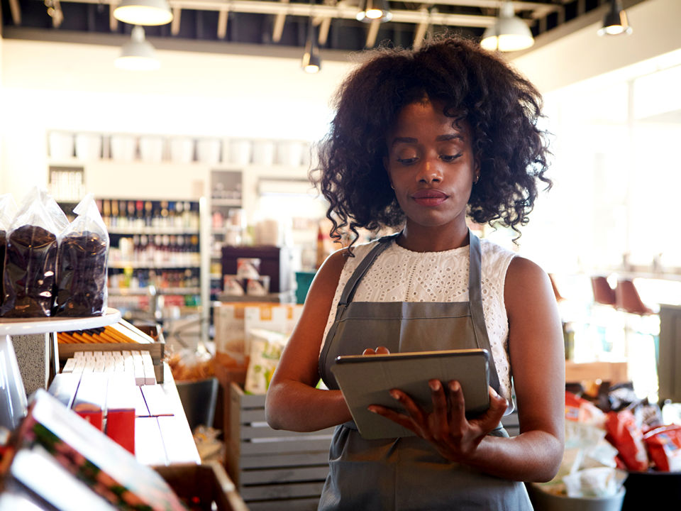 female manager in retail convenience store reviews store compliance data on electronic device
