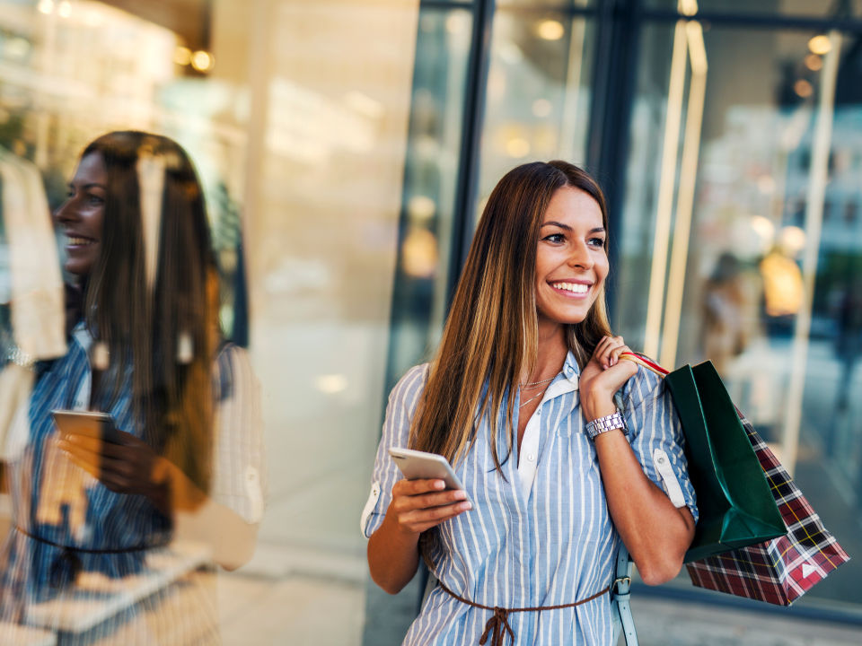 female shopper carrying several shopping bags and her smartphone looking in a retail store window