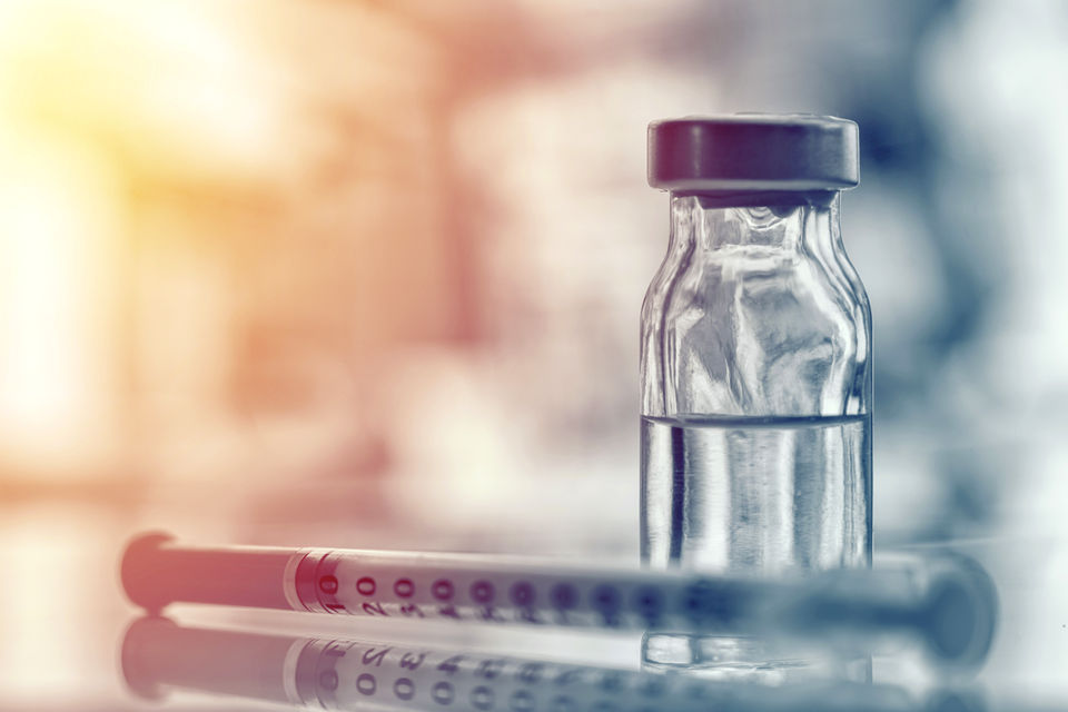 image of a vaccine vial next to a syringe with a heavily blurred retail pharmacy counter in the background