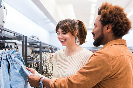 smiling male and female shoppers examining denim jeans on display in retail apparel store in shopping mall
