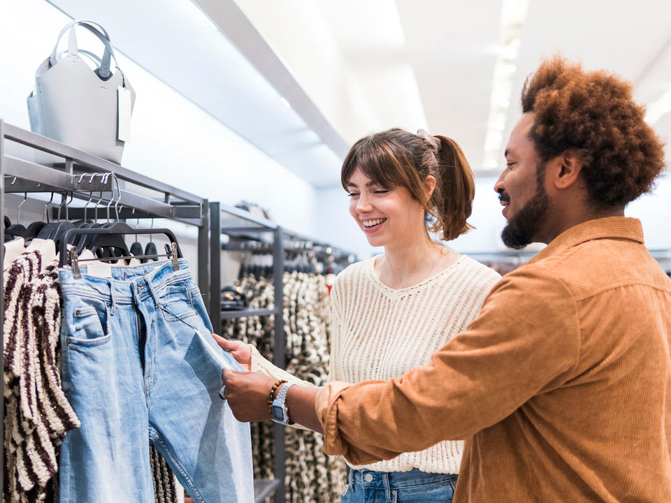 male retail store associate assistant clerk helps female shopper to select clothing from the apparel rack