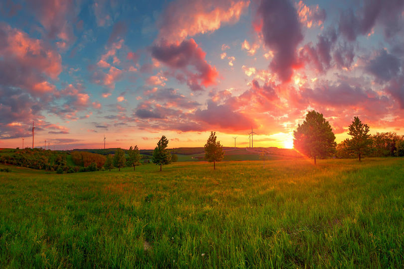 sunset over rural home with large fields of gass and scattered trees around the house with the sky a deepening blue and rose orange and gold tints to the clouds