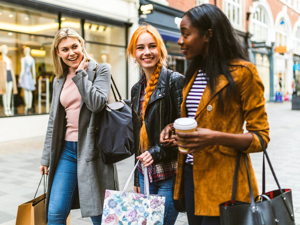 3 female shoppers chatting and carrying shopping bags while walking down the street in a retail shopping district